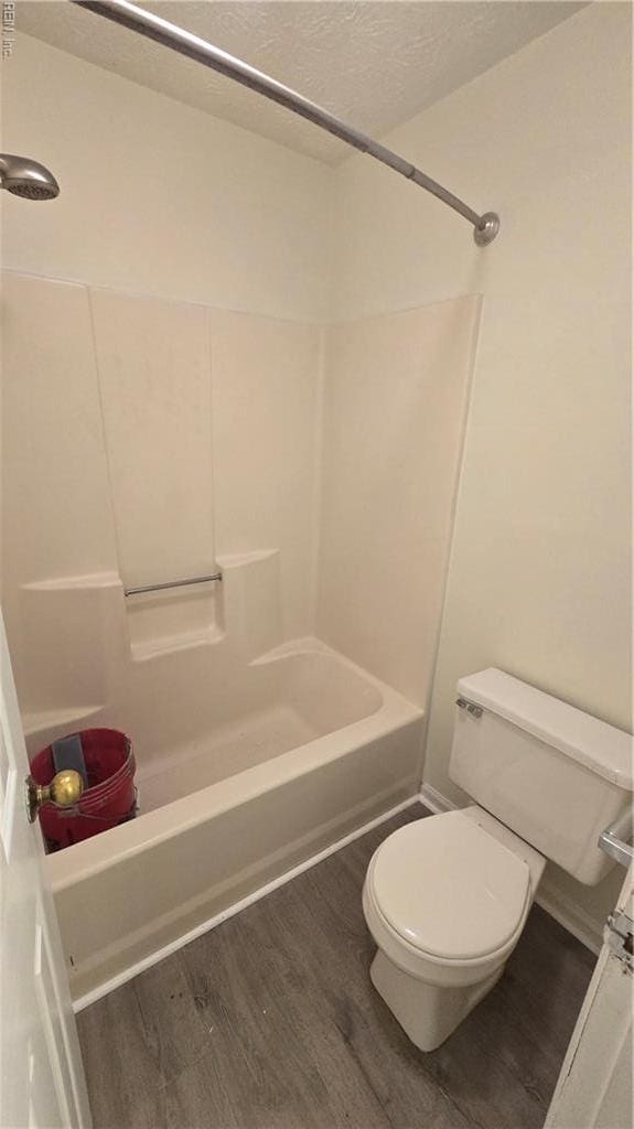 full bathroom featuring a textured ceiling, washtub / shower combination, toilet, and wood finished floors