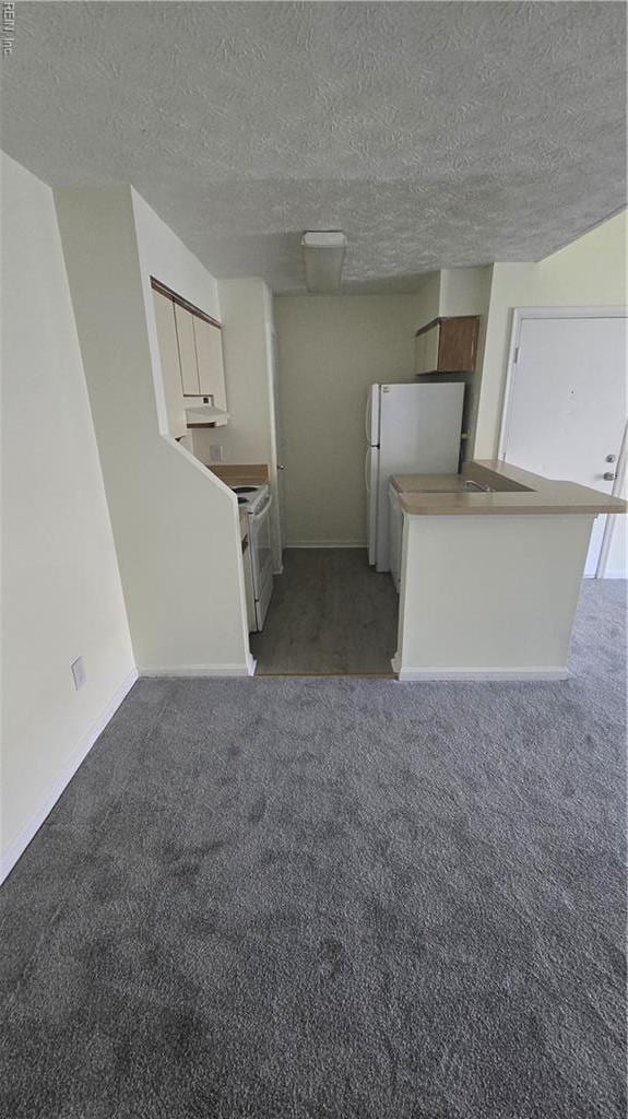 kitchen with white appliances, light carpet, baseboards, a textured ceiling, and white cabinetry