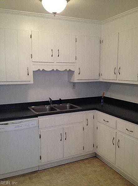 kitchen with white dishwasher, dark countertops, crown molding, a sink, and white cabinets