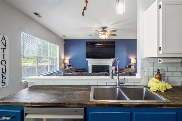 kitchen featuring blue cabinetry, dark countertops, stainless steel dishwasher, a sink, and open floor plan