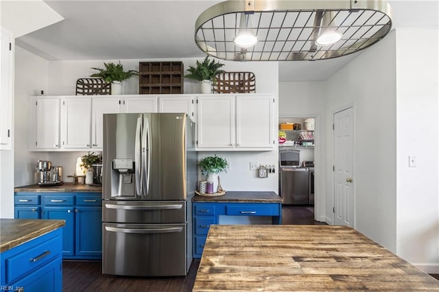 kitchen featuring independent washer and dryer, stainless steel fridge with ice dispenser, blue cabinetry, butcher block countertops, and white cabinetry