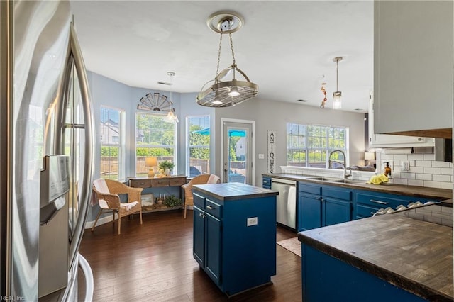 kitchen featuring appliances with stainless steel finishes, a sink, blue cabinetry, dark wood finished floors, and tasteful backsplash
