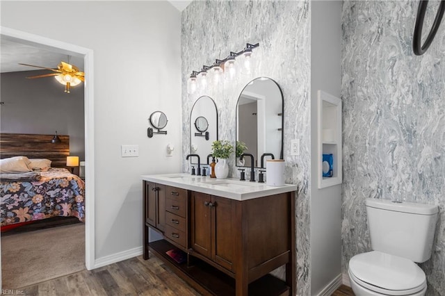 ensuite bathroom featuring double vanity, a ceiling fan, wood finished floors, toilet, and a sink
