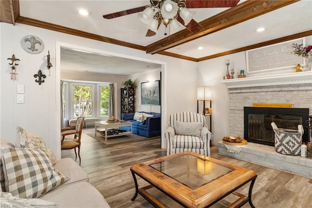 living area with ornamental molding, wood finished floors, a fireplace, beamed ceiling, and ceiling fan
