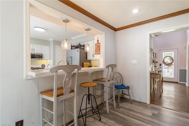 interior space featuring crown molding, high end refrigerator, stainless steel microwave, decorative light fixtures, and wood finished floors