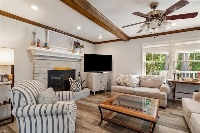 living area featuring ornamental molding, wood finished floors, a fireplace, beamed ceiling, and ceiling fan