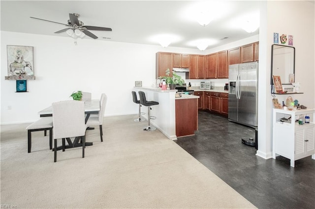 kitchen featuring a peninsula, a kitchen bar, light countertops, under cabinet range hood, and stainless steel appliances