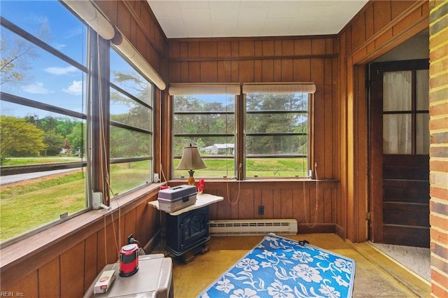sunroom / solarium featuring a baseboard radiator, wooden walls, and a wood stove