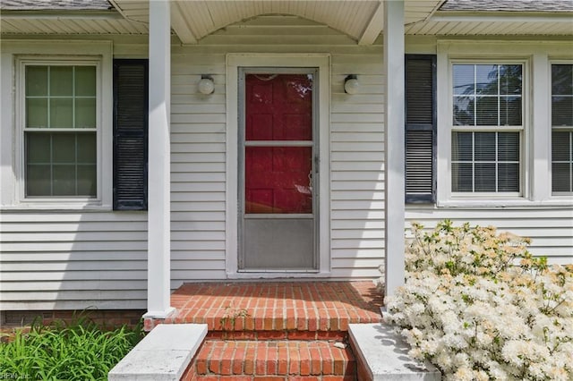 view of exterior entry featuring covered porch and a shingled roof