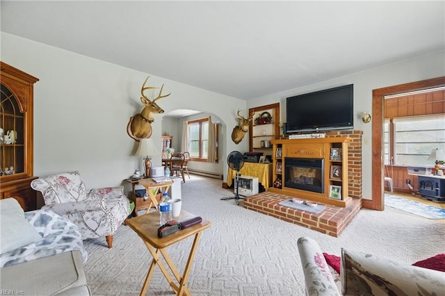 living area featuring a glass covered fireplace, arched walkways, baseboard heating, and carpet flooring