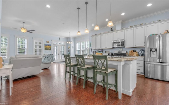kitchen with a breakfast bar area, appliances with stainless steel finishes, open floor plan, ornamental molding, and an island with sink