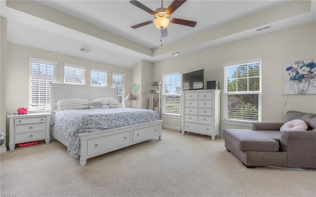 carpeted bedroom with a raised ceiling, multiple windows, ceiling fan, and visible vents