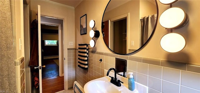bathroom featuring a sink, ornamental molding, baseboard heating, and a wainscoted wall