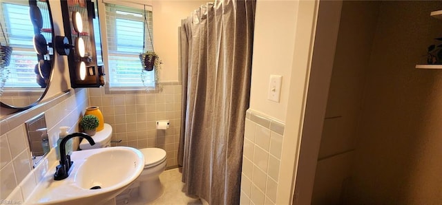 bathroom with curtained shower, toilet, tile walls, a wainscoted wall, and a sink