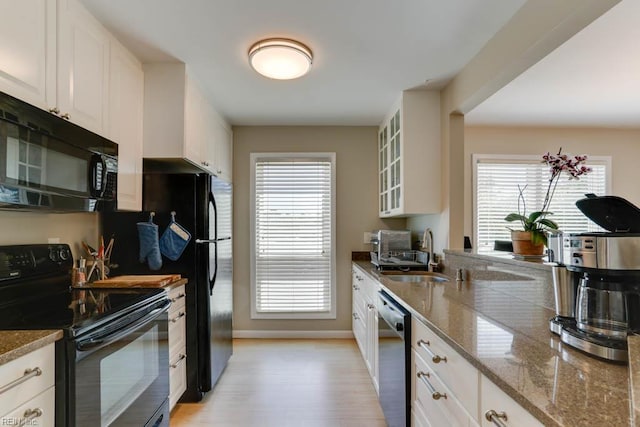 kitchen with a sink, light wood-style flooring, white cabinetry, glass insert cabinets, and black appliances