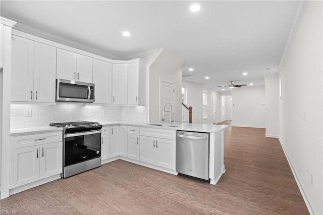 kitchen with backsplash, appliances with stainless steel finishes, a sink, light countertops, and a peninsula