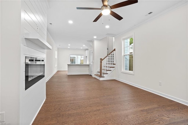 unfurnished living room featuring ornamental molding, dark wood-style flooring, ceiling fan, and stairway