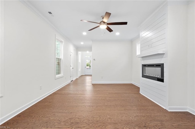 unfurnished living room featuring ceiling fan, crown molding, a large fireplace, wood finished floors, and baseboards