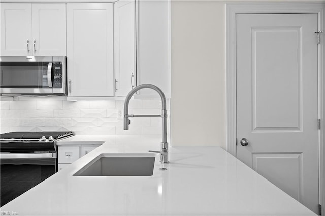 kitchen with a sink, appliances with stainless steel finishes, white cabinetry, and light countertops
