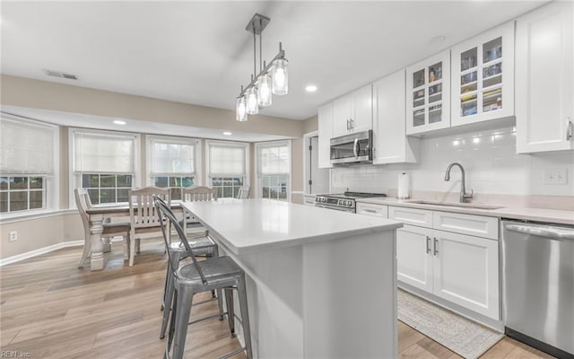 kitchen featuring light countertops, white cabinets, a sink, light wood-style flooring, and appliances with stainless steel finishes