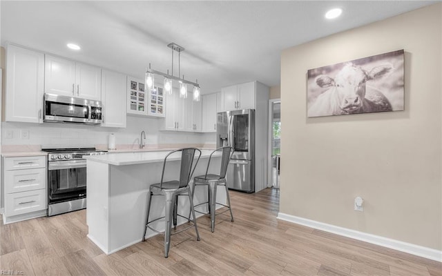 kitchen featuring a kitchen bar, light countertops, white cabinetry, light wood finished floors, and appliances with stainless steel finishes
