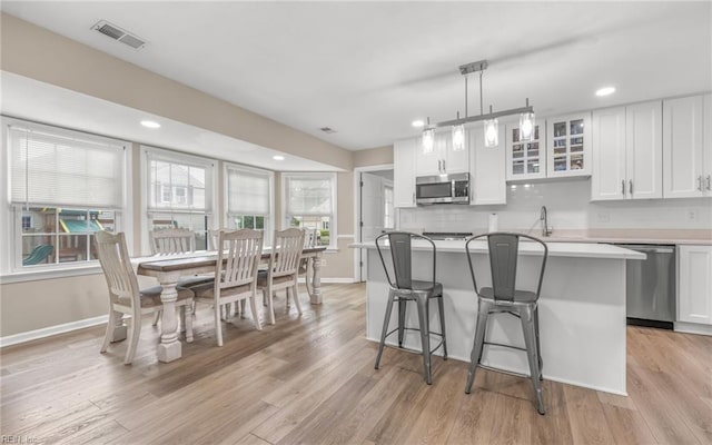 kitchen with a kitchen breakfast bar, visible vents, white cabinets, stainless steel appliances, and an island with sink