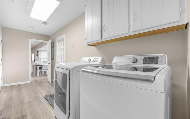 laundry room with light wood-style floors, separate washer and dryer, baseboards, and cabinet space