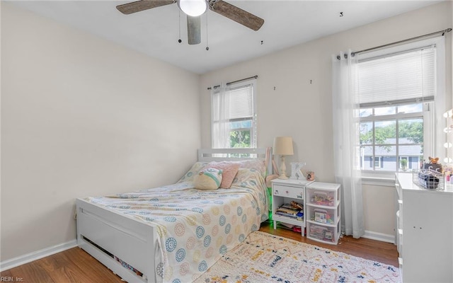 bedroom with baseboards, wood finished floors, and multiple windows