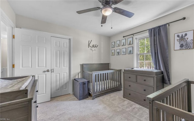 carpeted bedroom with a crib, a ceiling fan, and a closet
