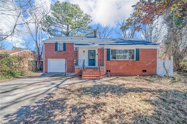 split level home with driveway, a chimney, a garage, brick siding, and fence