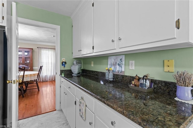 kitchen featuring crown molding, white cabinetry, marble finish floor, and dark stone countertops
