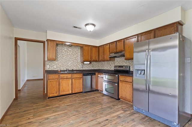 kitchen featuring visible vents, dark countertops, under cabinet range hood, backsplash, and stainless steel appliances