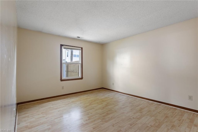 unfurnished room featuring a textured ceiling, visible vents, baseboards, and light wood finished floors