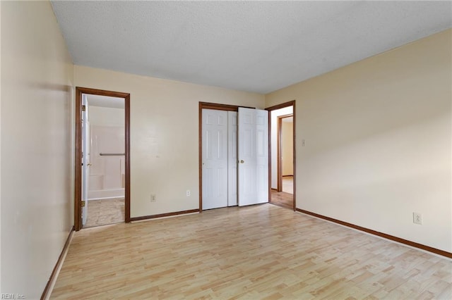 unfurnished bedroom featuring a closet, light wood-style floors, baseboards, ensuite bathroom, and a textured ceiling