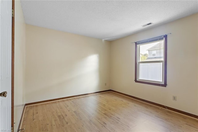 empty room featuring wood finished floors, baseboards, a textured ceiling, and visible vents
