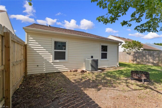 back of property with a fenced backyard, central AC unit, a lawn, and a fire pit