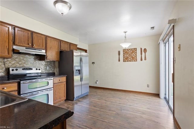 kitchen with decorative backsplash, dark countertops, wood finished floors, under cabinet range hood, and stainless steel appliances