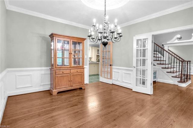 unfurnished dining area featuring a notable chandelier, french doors, stairway, and wood finished floors