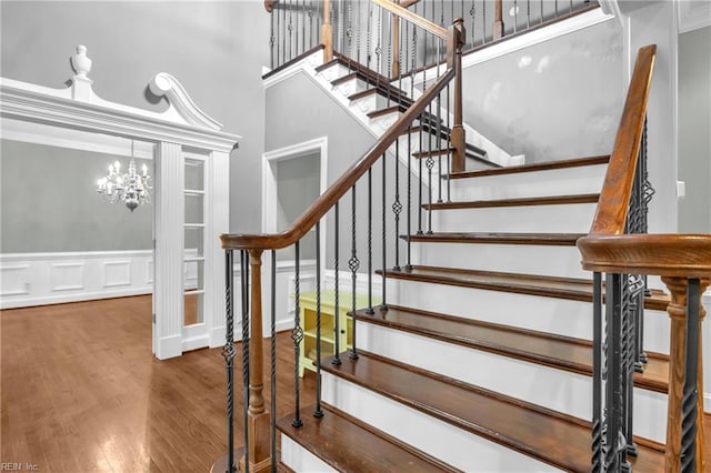 stairs with a towering ceiling, wood finished floors, and a notable chandelier