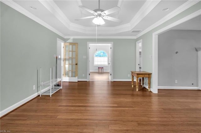 unfurnished room with baseboards, ceiling fan, a tray ceiling, and wood finished floors