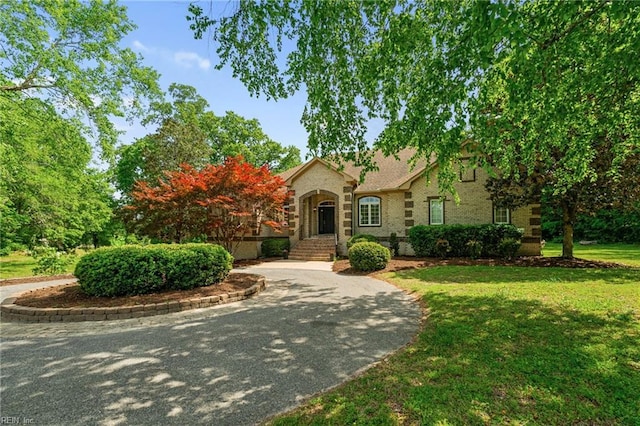 view of front of property featuring brick siding, a front lawn, and curved driveway