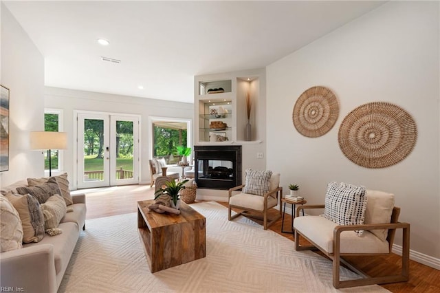 living room featuring a multi sided fireplace, visible vents, wood finished floors, baseboards, and recessed lighting