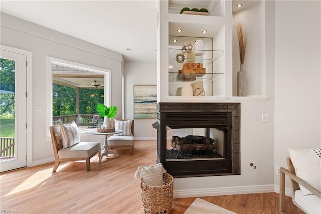 living area with a multi sided fireplace, baseboards, and light wood-style floors