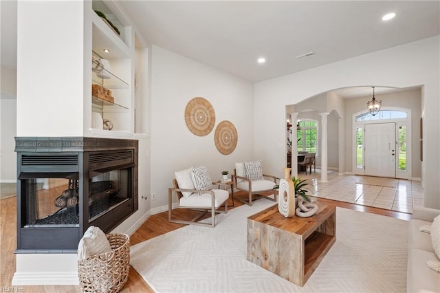 living room featuring a multi sided fireplace, arched walkways, wood finished floors, baseboards, and ornate columns