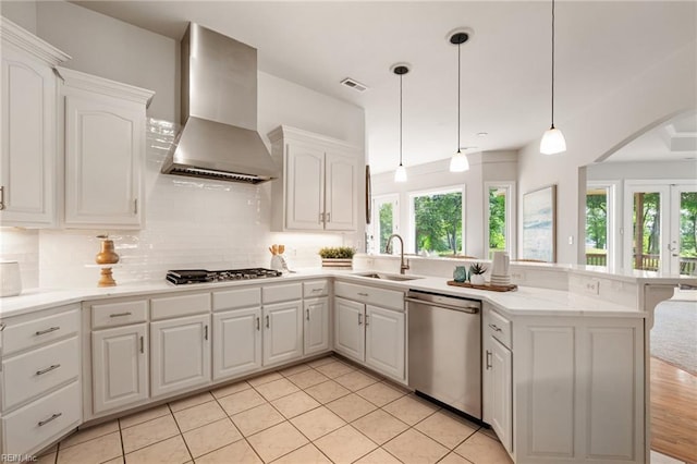 kitchen with wall chimney range hood, dishwasher, a sink, a peninsula, and a wealth of natural light