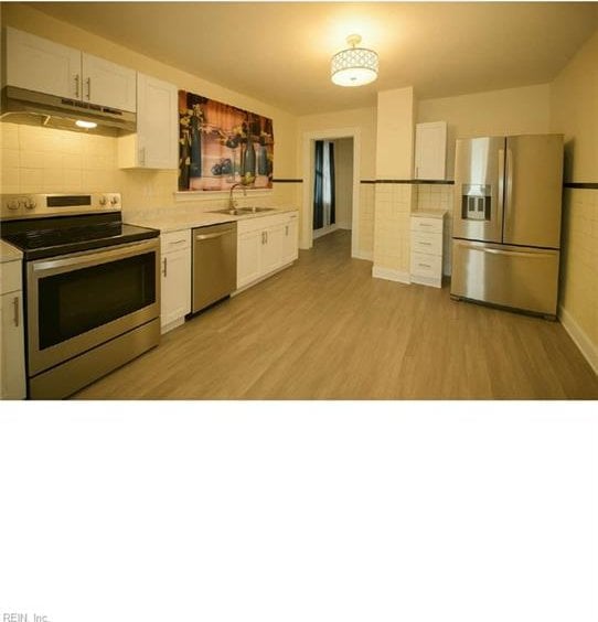 kitchen featuring light countertops, under cabinet range hood, a sink, light wood finished floors, and appliances with stainless steel finishes