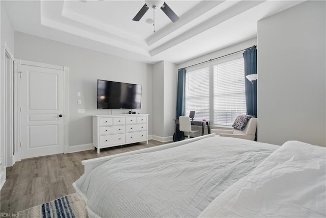 bedroom with baseboards, ceiling fan, wood finished floors, and a tray ceiling