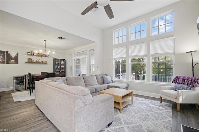 living area featuring baseboards, ceiling fan with notable chandelier, wood finished floors, and visible vents