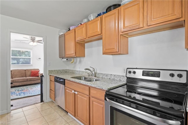 kitchen featuring light tile patterned flooring, appliances with stainless steel finishes, light stone counters, a sink, and a ceiling fan