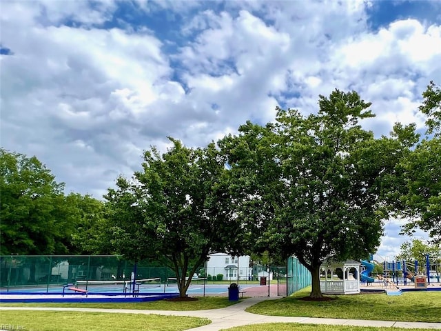 view of community with a lawn, fence, playground community, and a tennis court